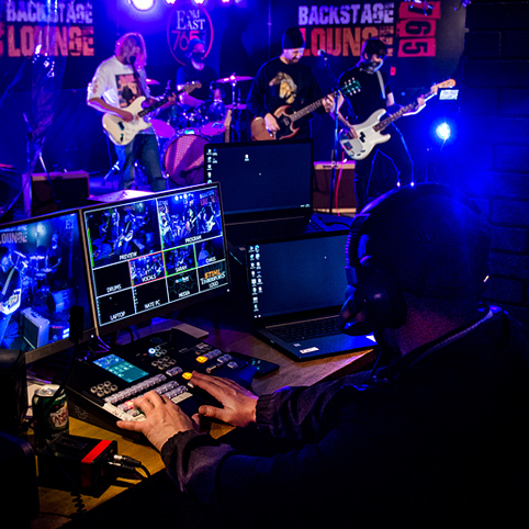 person sitting at desk controlling song board with band on stage playing guitars