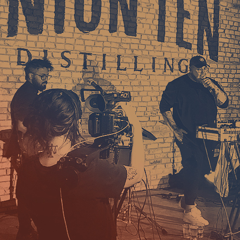 A musical duo performing on stage in London, Ontario being filmed by a by a female videographer